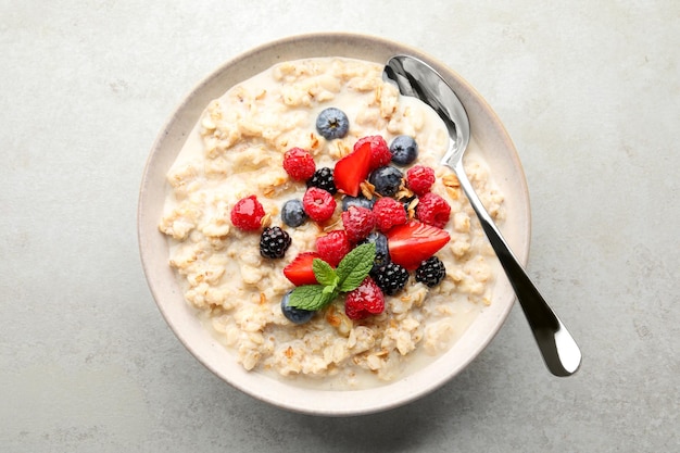 Bowl of oatmeal porridge served with berries on light grey table top view