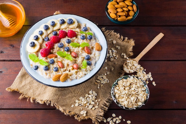 Bowl of oatmeal porridge with berries honey and fruits on burlap Tasty oatmeal with raspberries