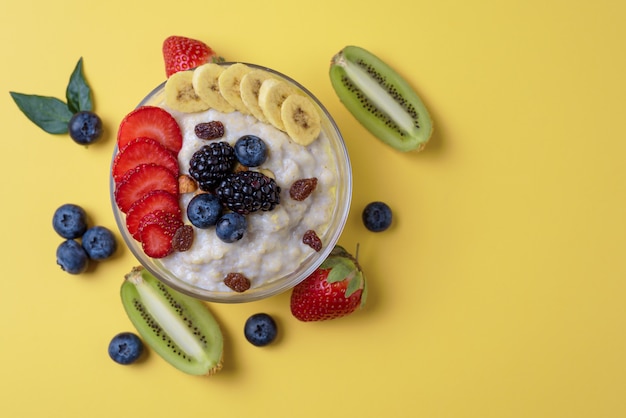 bowl of oatmeal, strawberries, blueberries, kiwis and blackberries on yellow background