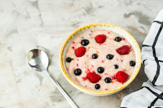 A bowl of oatmeal with raspberries and blueberries on a gray table