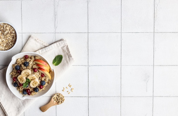 A bowl of oatmeal with a spoon on a white tile background.