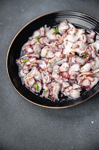 A bowl of octopus salad with green herbs on a grey table.