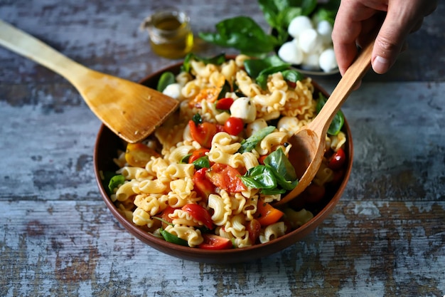 A bowl of pasta salad with a wooden spoon in it.