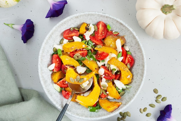 A bowl of peach salad with a spoon scooping up a slice of peaches, feta, and pumpkin on a table.