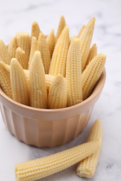 Bowl and pickled baby corn on white marble table closeup