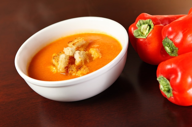 A bowl of red pepper cream soup served on a wooden surface