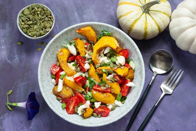 A bowl of roasted squash salad with a pumpkin and a spoon.