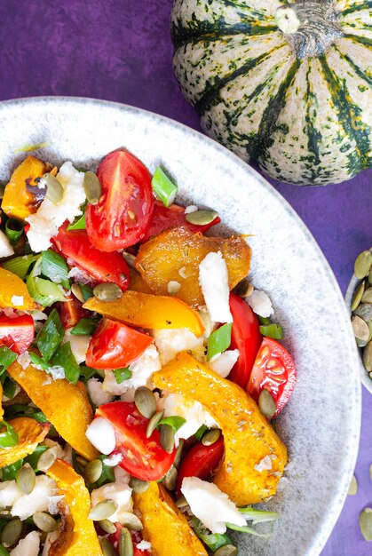 A bowl of roasted vegetables with pumpkins on the side.