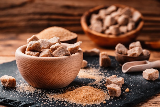 Bowl and scoop with sand and lump brown sugar on wooden background brown sugar cube Make unhealthy nutrition obesity diabetes dental care and much more