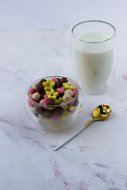 A bowl of snacks in the shape of a ball hearts and flowers on a white marble table Breakfast cereal and a glass of milk