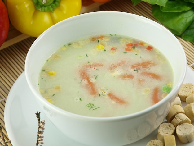 A bowl of soup with vegetables on a plate.