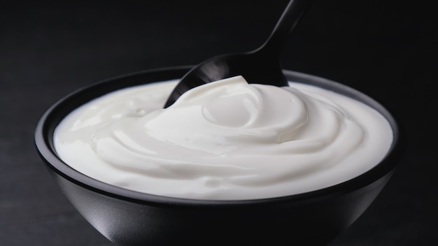 Bowl of sour cream on black, greek yogurt with spoon