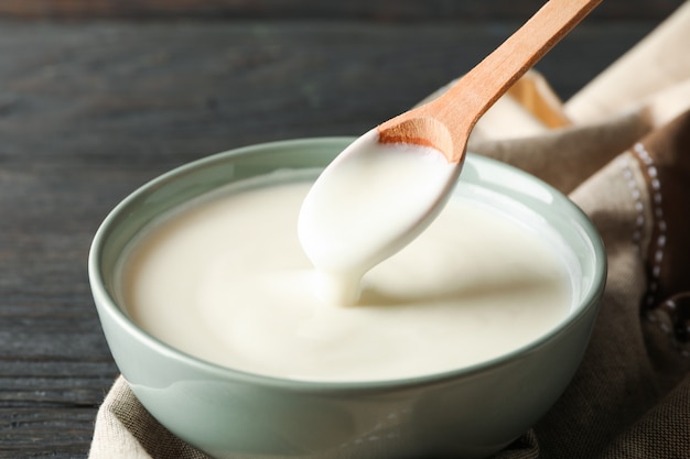 Bowl of sour cream yogurt, spoon and towel on wooden background