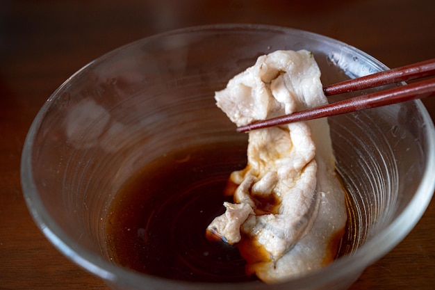 A bowl of soy sauce with chopsticks holding a piece of food.