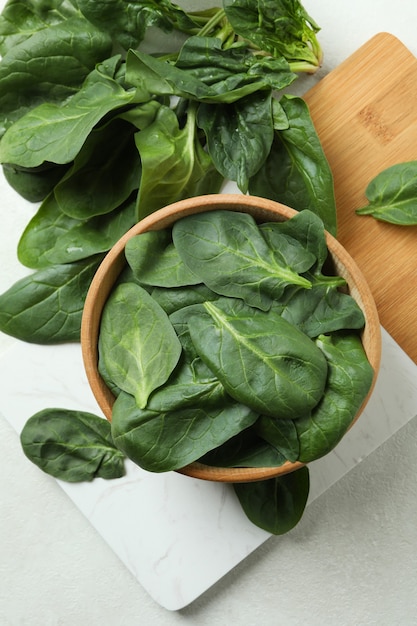 Bowl of spinach on board, on white textured table