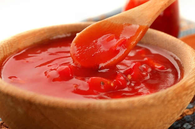 Bowl and spoon with tasty chili sauce on table closeup