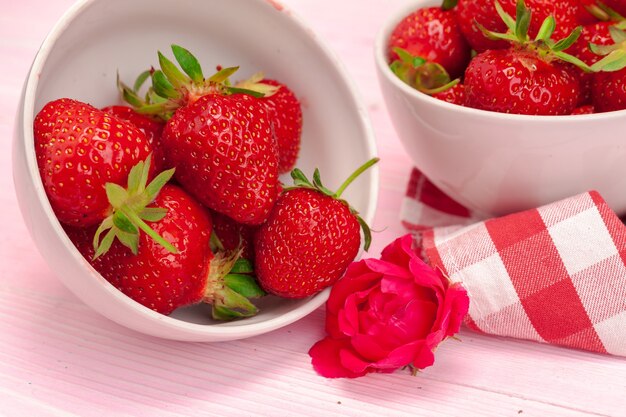 Bowl of strawberry harvest on wooden table close up