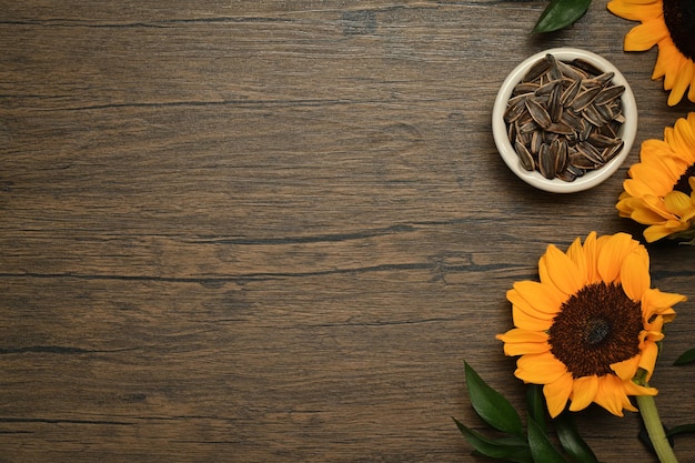 Bowl of sunflower seeds and yellow sunflowers on rustic wooden background Top view with copy space for your text