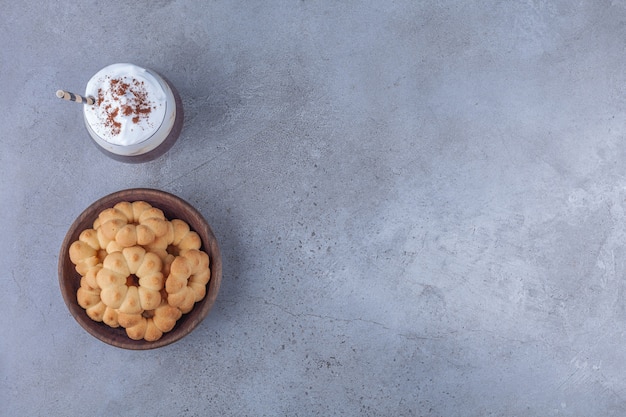 Bowl of sweet biscuits with glass of coffee on marble background. 