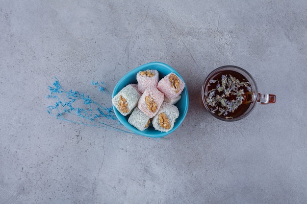 Bowl of sweet delights with walnuts and cup of hot tea on stone background. 