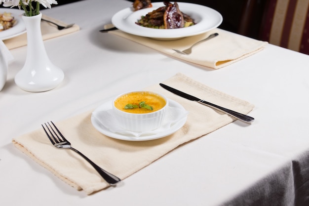 Bowl of tasty autumn pumpkin soup served at a dinner table with assorted other appetizers in a restaurant