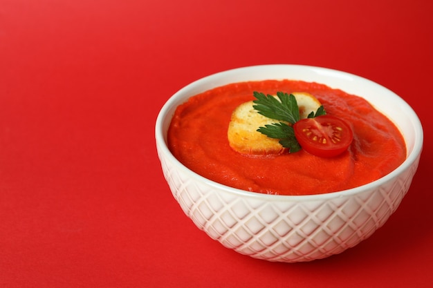 Bowl of tasty Gazpacho soup on red background