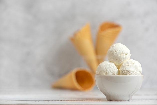 Bowl of vanilla ice cream and waffle cones on light.