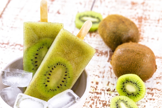 Bowl of vanilla and kiwi yogurt popsicles on white rustic wooden table