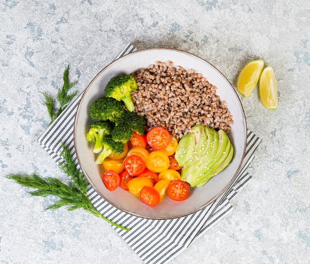 A bowl of vegan food, a vegan dinner of boiled buckwheat, colored tomatoes, avocado and broccoli. Top view