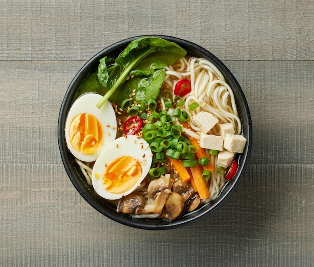 bowl of vegetarian asian ramen noodle soup on wooden background top view