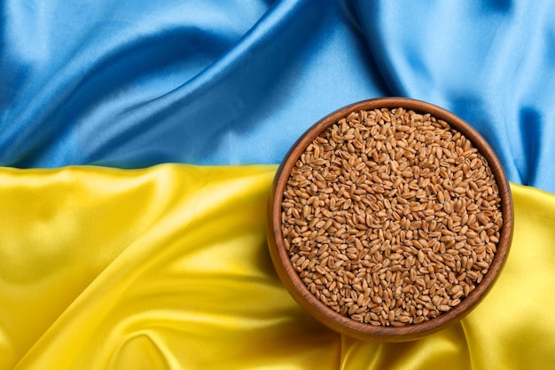 Bowl of wheat grains on Ukrainian flag top view Space for text