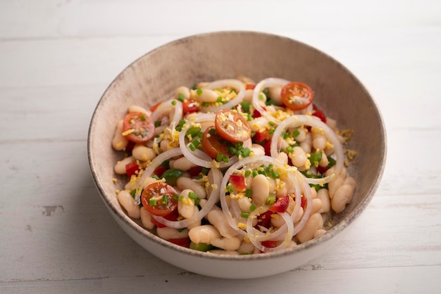 A bowl of white beans with tomatoes onions and cilantro