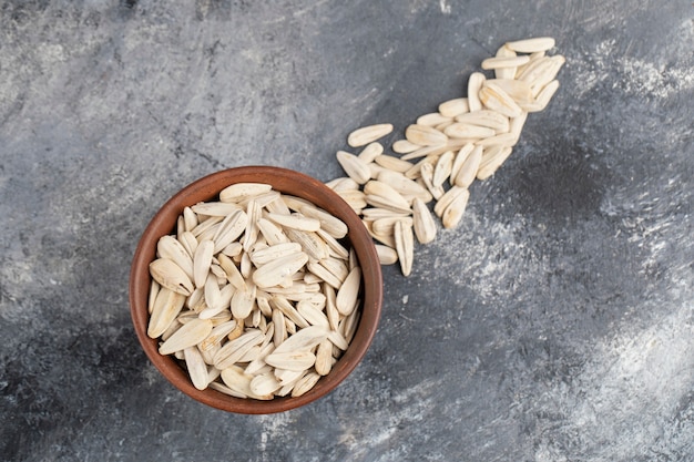 Bowl of white sunflowers seeds scattered on marble surface.