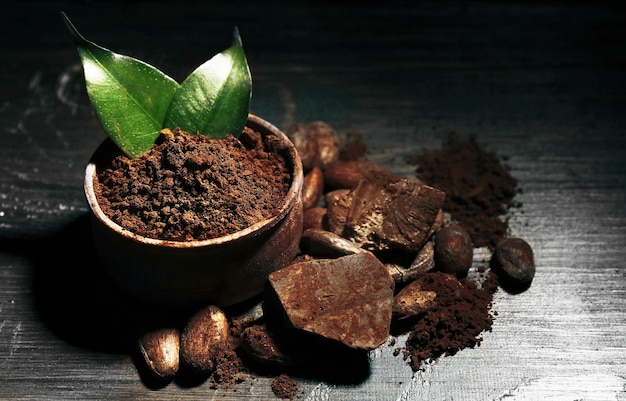 Bowl with aromatic cocoa powder and green leaf on wooden background close up