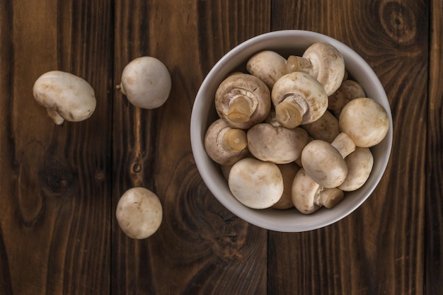 A bowl with champignons and three separate mushrooms on a wooden background