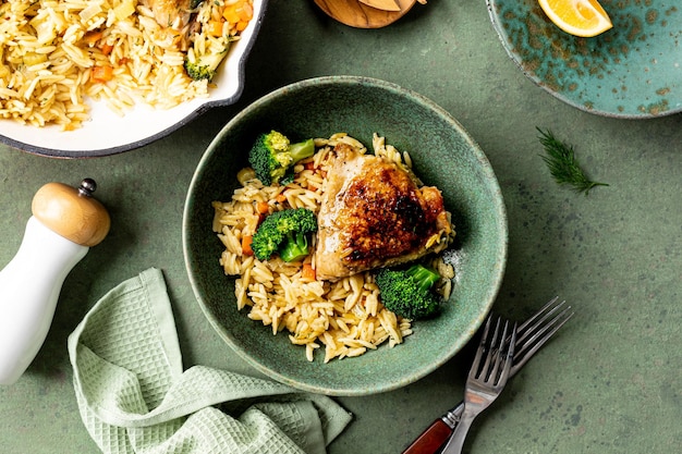 Bowl with chicken pasta orzo with vegetables in Mediterranean style on a green background