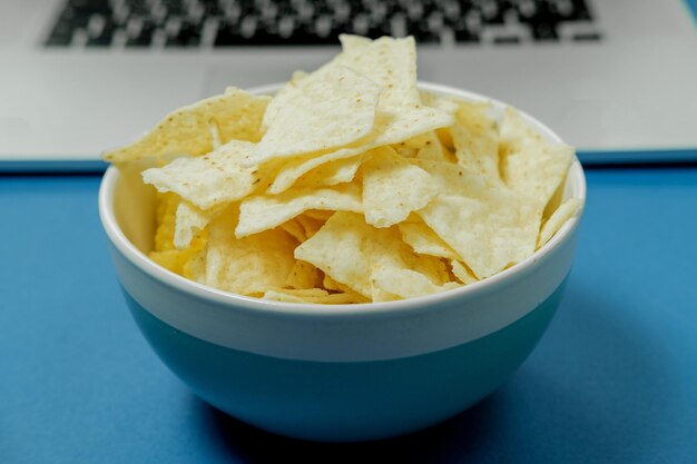 Bowl with chips on a laptop background on a blue background Bad habits concept