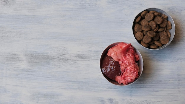 Bowl with dog biscuits and with raw meat on a wooden table. Barf diet for dogs