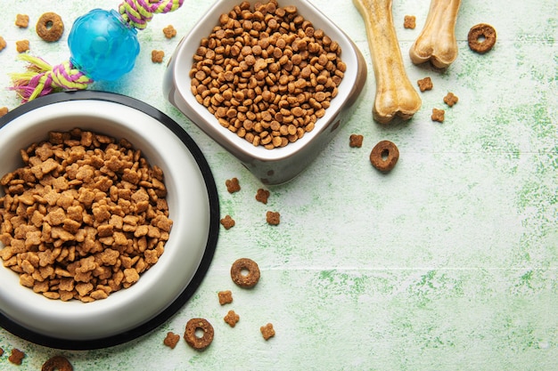 A bowl with dog food dog treats and toys on a wooden floor