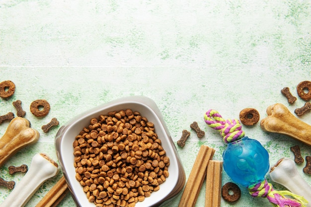 A bowl with dog food dog treats and toys on a wooden floor