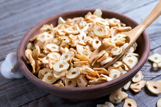 Bowl with dried garlic flakes on wooden background