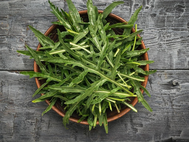 A bowl with fresh green arugula leaves on a black wooden table Flat lay