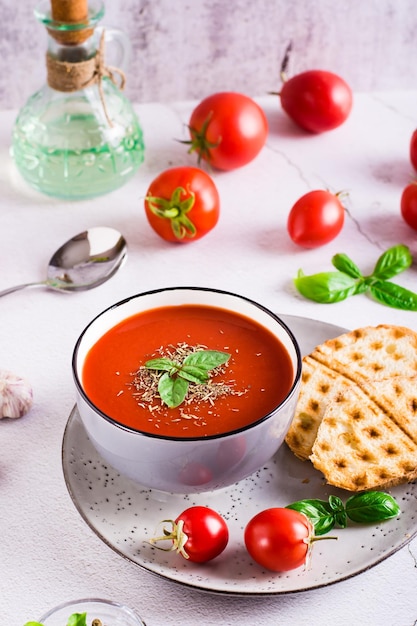 Bowl with homemade tomato soup with basil and fresh vegetables on the table Vertical view