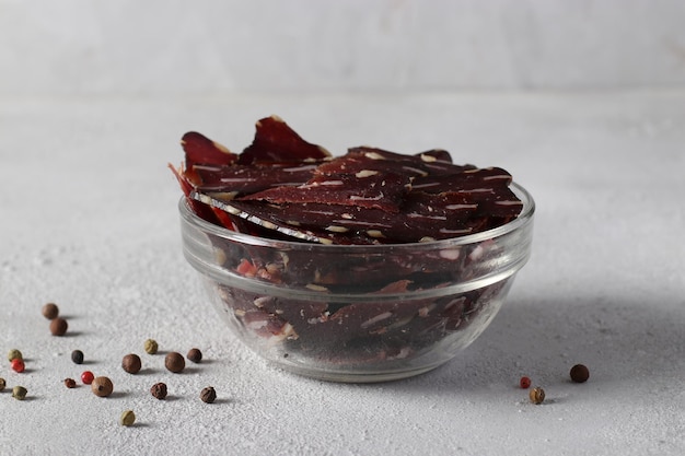 Bowl with jerky meat and peppers on light gray background Closeup