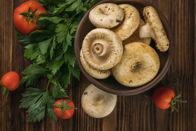 A bowl with large wild mushrooms vegetables and celery leaves on a wooden table Flat lay