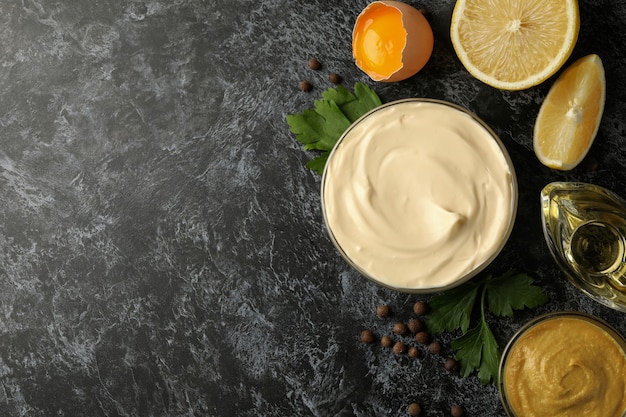 Bowl with mayonnaise and ingredients for cooking on black smokey background