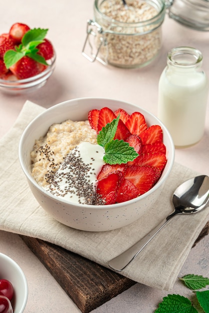 Bowl with oatmeal, fresh strawberries and chia seeds on a soft pink background. Close-up, vertical.