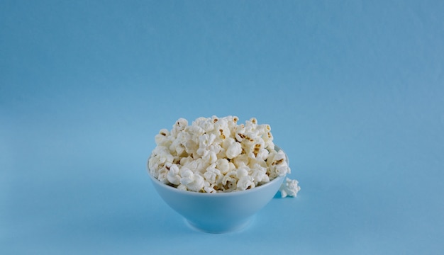 Bowl with popcorn on blue background.