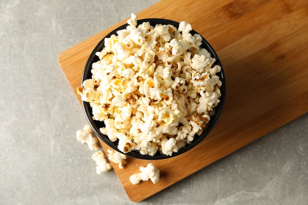 Bowl with popcorn and board on grey background