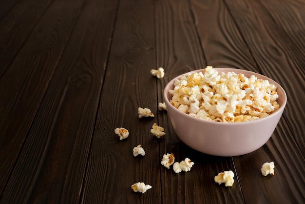 Bowl with popcorn on dark wooden table with copyspace